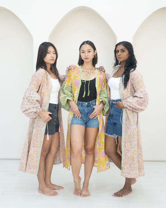 Three women standing together wearing overcoats against a white background